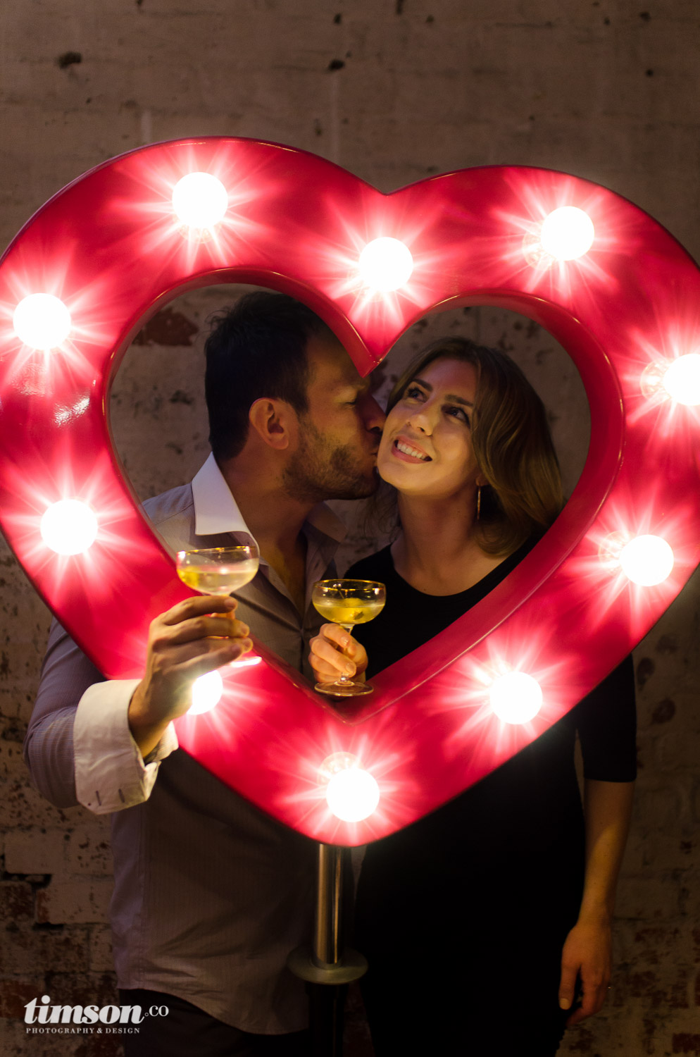 Denis & Emma Merkas, co-founders of Melt: Massage for Couples share a kiss in the Pink Carnival Heart from Letter Lights